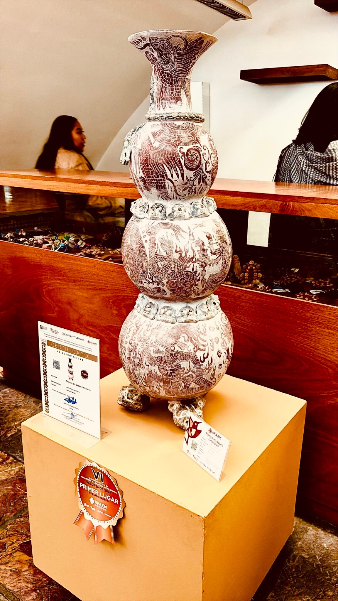Florero de barro bruñido de 80 centímetros de alto formado por tres cuerpos esféricos con iconografía prehispánica incisa y bandas de cráneos, obra de Juan Luis Galicia Rivero, de Teotihuacán